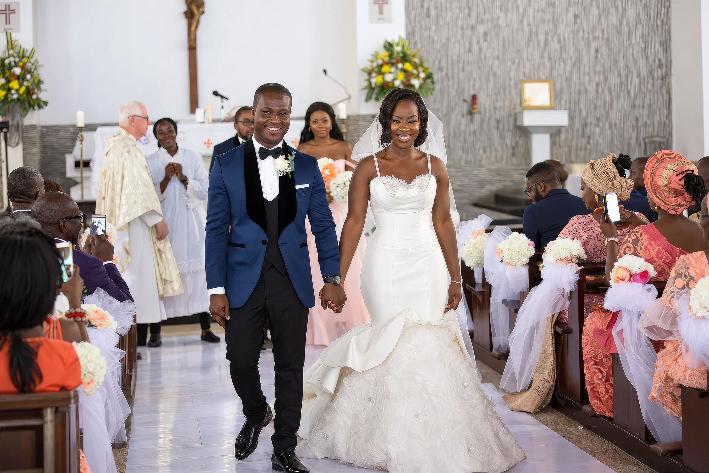 Nana Ama and her husband walk back down the aisle after their church ceremony in Accra, Ghana. Her bespoke Kosibah couture gown has a draped cowl neckline, embellished straps and a figure-hugging silhouette flaring into a trumpet skirt.
