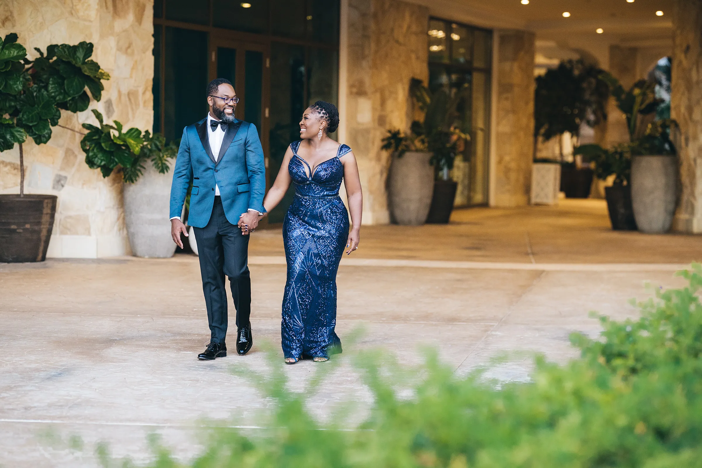 Nana, in a midnight-blue sequinned lace Kosibah gown, and her husband, in a teal tuxedo jacket, walk out of the hotel lobby in Florida.