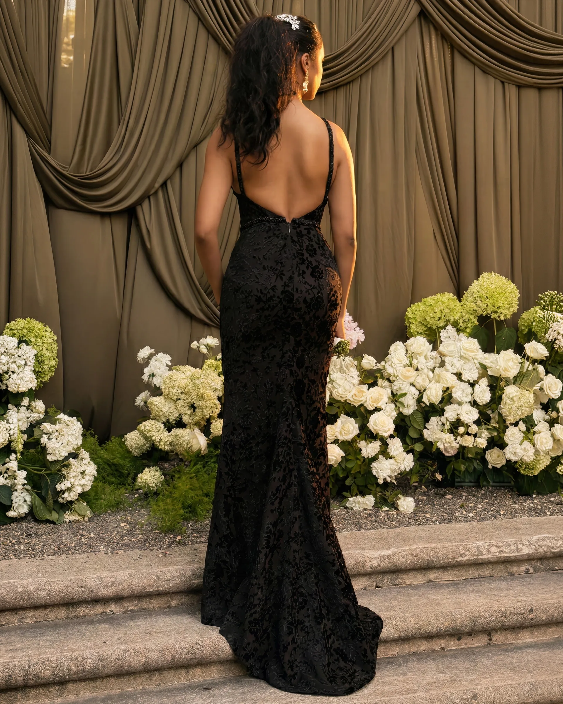 Ebony, back: fine straps frame a deeply scooped open back, and the patterned velvet runs close over the hips to a short train on the steps.