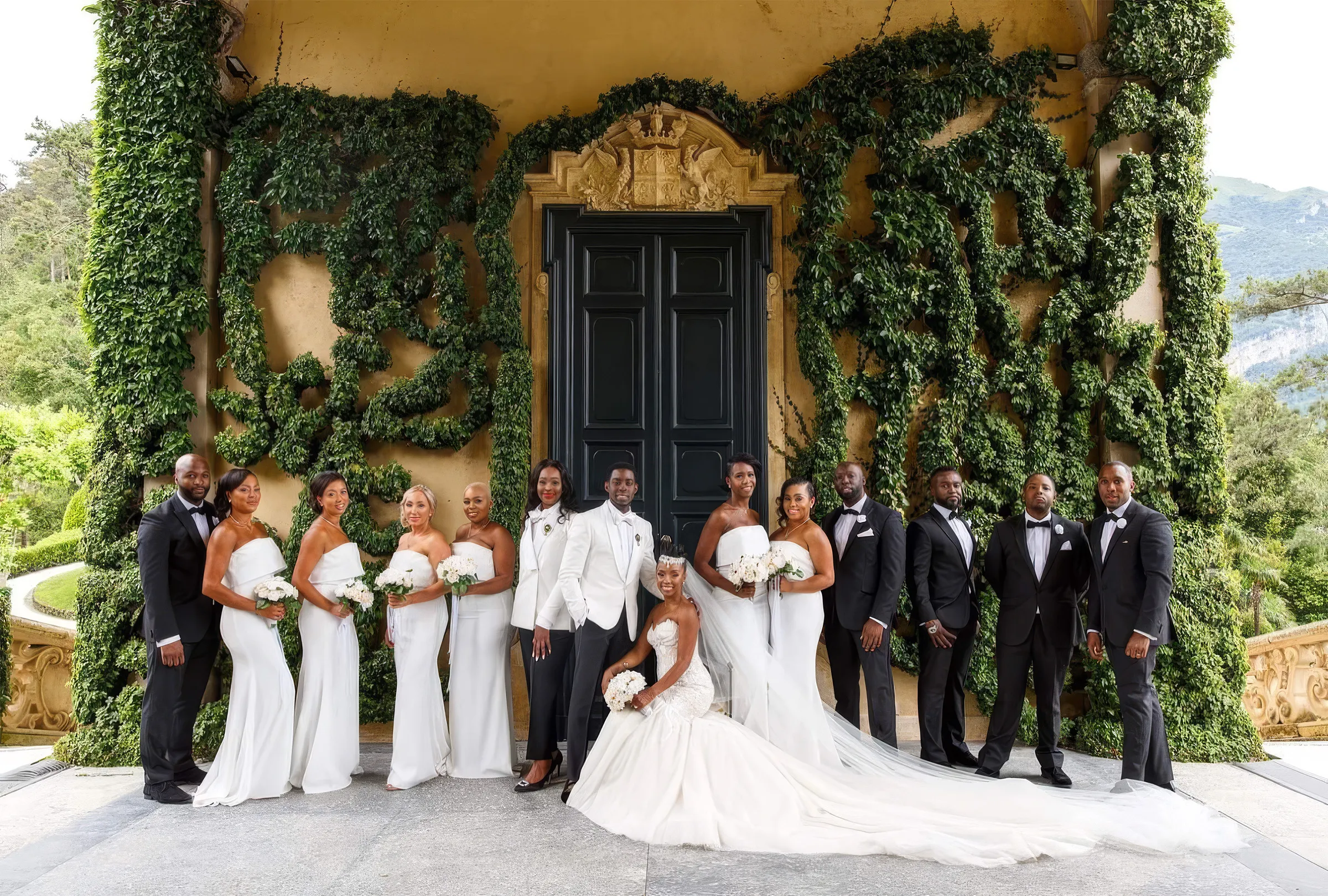 Denise, seated in her couture mermaid gown with a layered tulle skirt and a 2.5-metre train spread across the terrace, poses with her husband, bridesmaids in white and groomsmen in black tie at Lake Como, Italy.