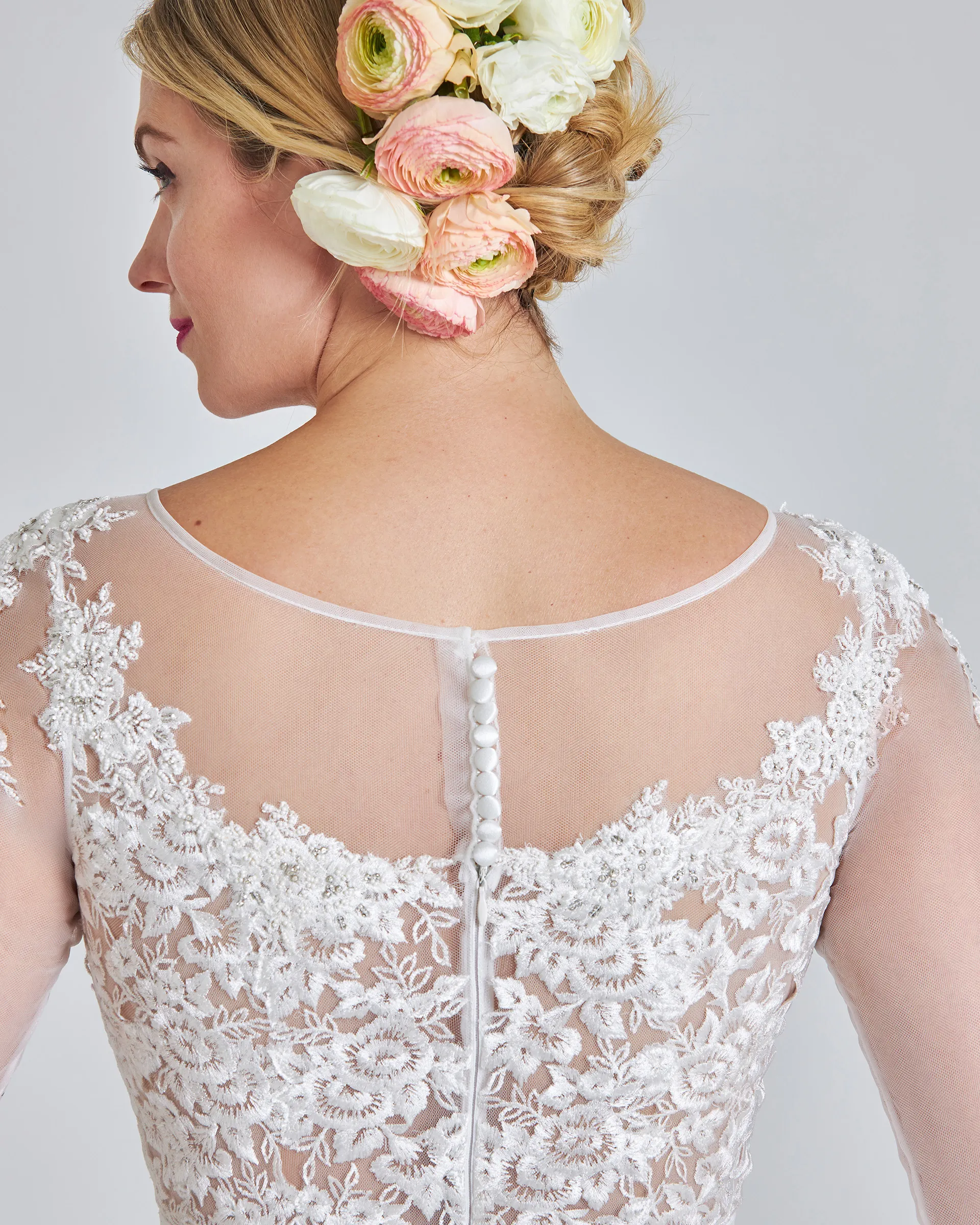 Ariyike, back detail: covered buttons down sheer tulle between scalloped lace, with pink ranunculus pinned in her hair.