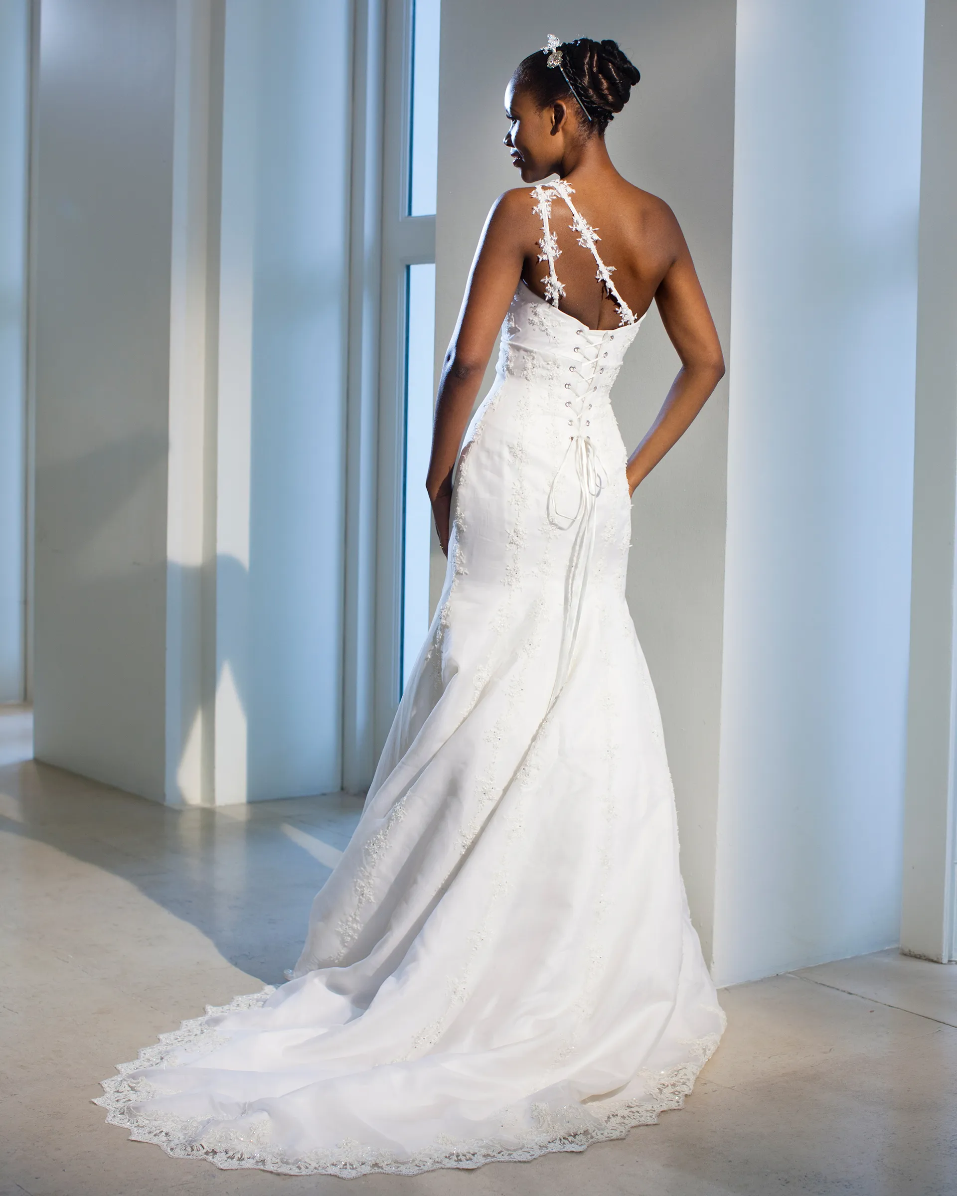 Aurora, back: lace and crystal appliqués form the shoulder strap, the bodice laces up the back, and the fishtail skirt pools into a lace-edged train.
