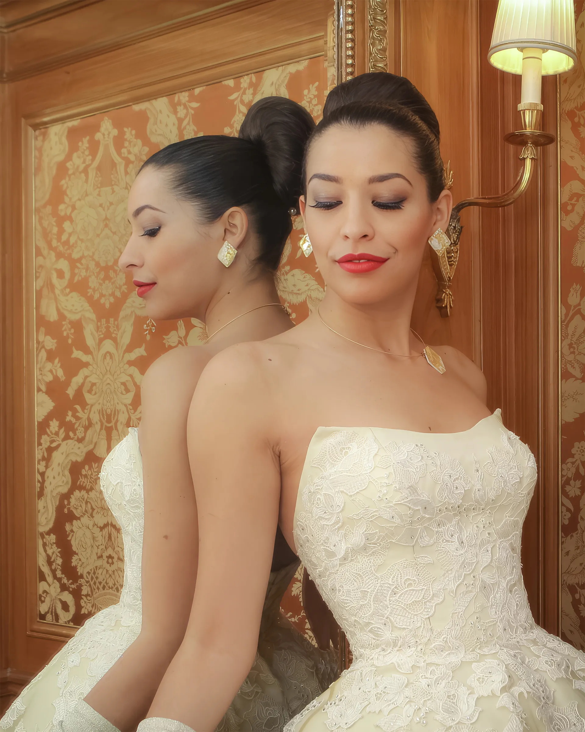 Clio, front detail, eyes closed beside her reflection in a gilt mirror: crystal-embellished guipure lace across the strapless corseted bodice.