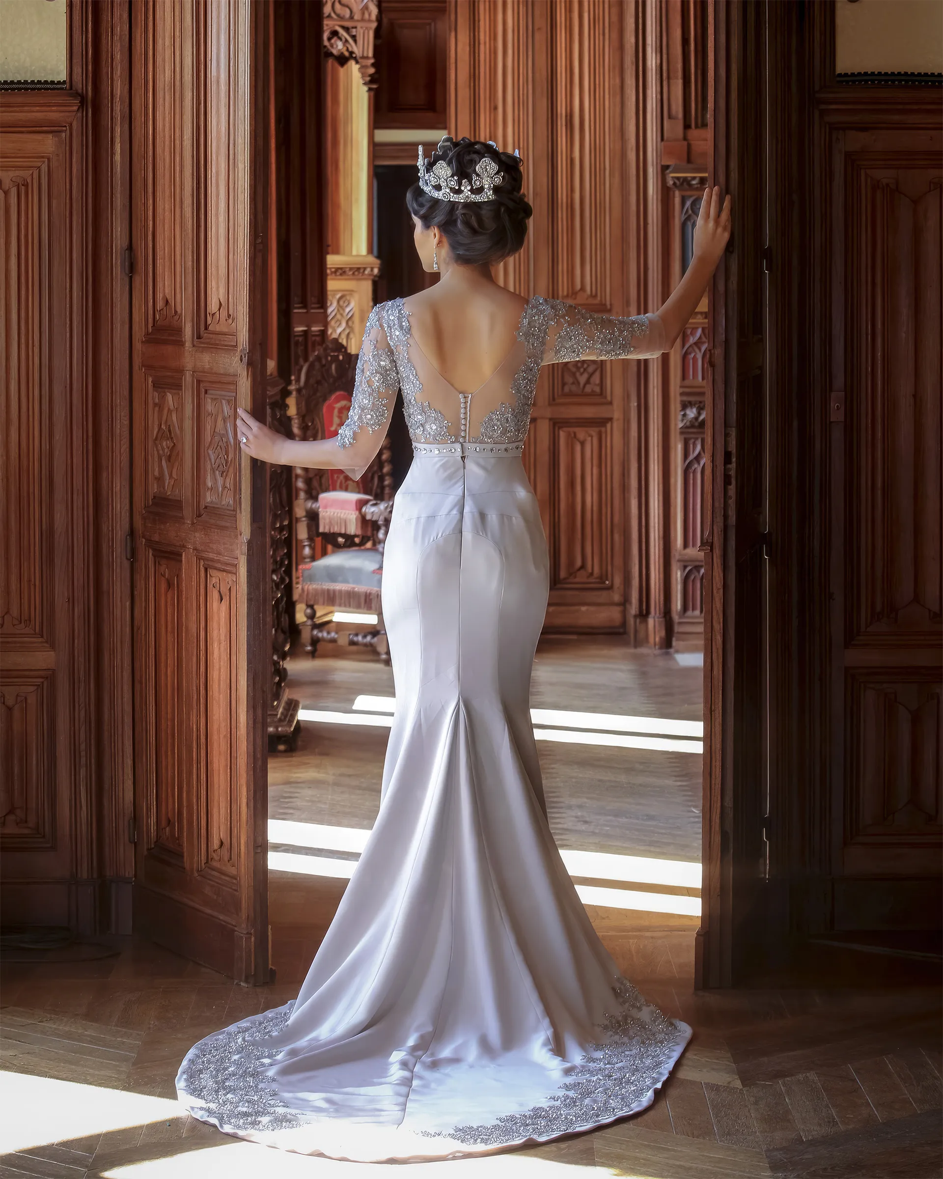 Erato framed in carved wooden doors, arms outstretched: the beaded illusion back, the trumpet skirt and the appliquéd hem of the train.