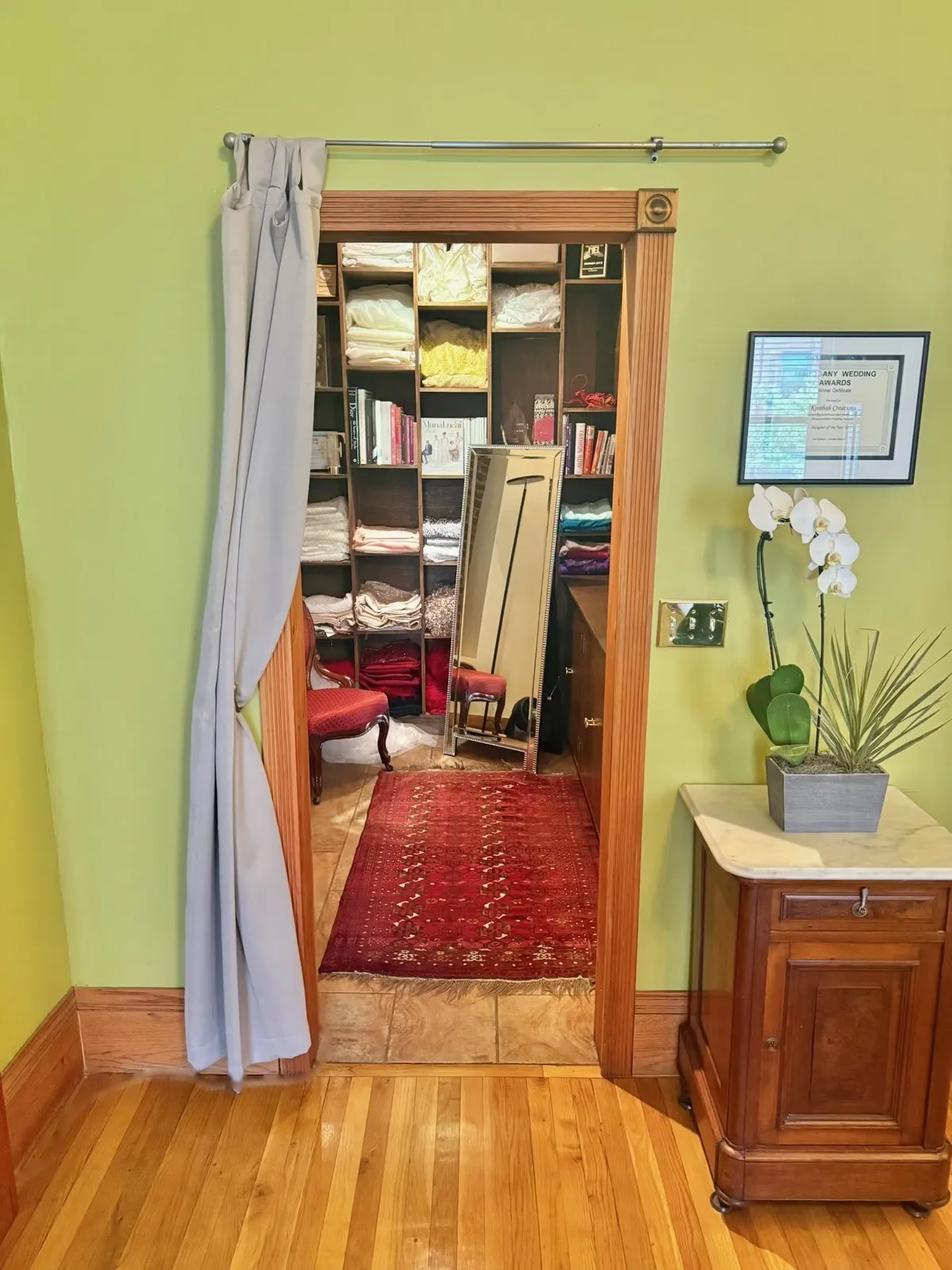 A curtained doorway from the salon into the changing room, with shelves of fabrics and books and a red Persian runner.