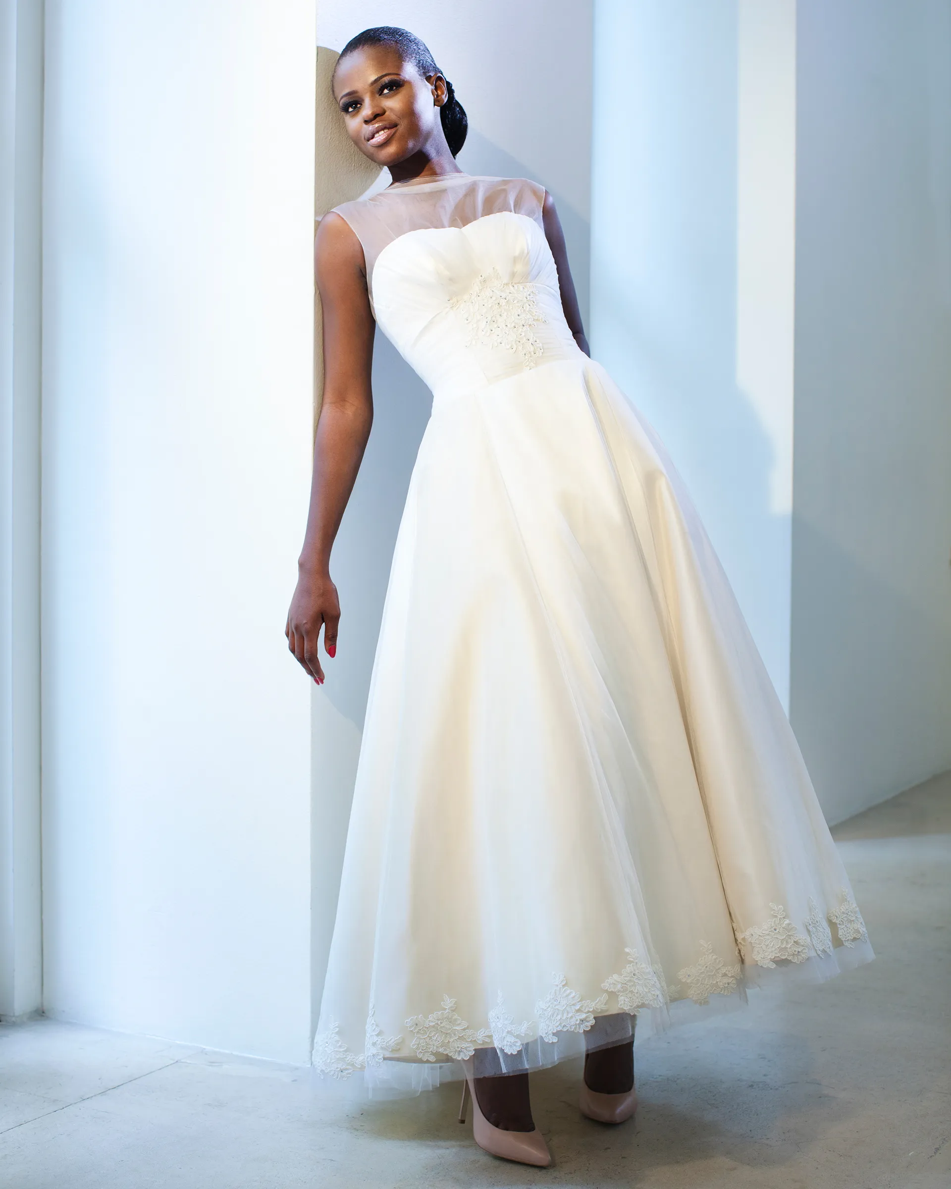 Giselle leaning on a wall: the sheer tulle chemise, beaded lace at the waist and the full ivory skirt with a lace-edged hem above pale heels.