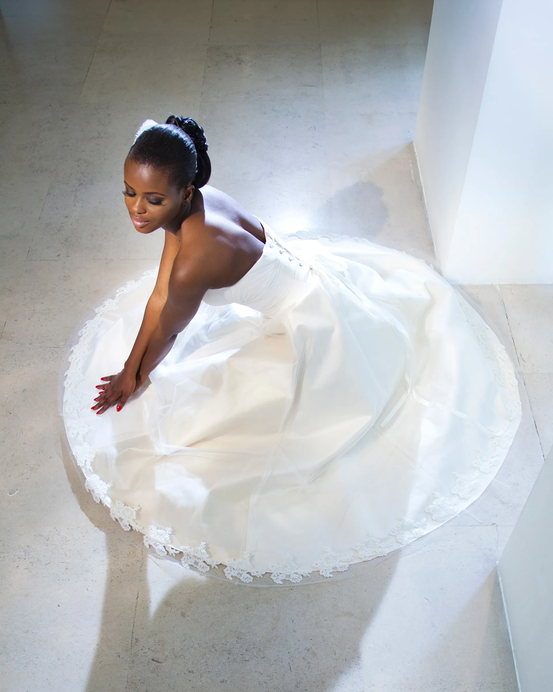 Giselle from above, kneeling on a stone floor with the full skirt spread in a circle around her, its lace-edged hem forming a ring.