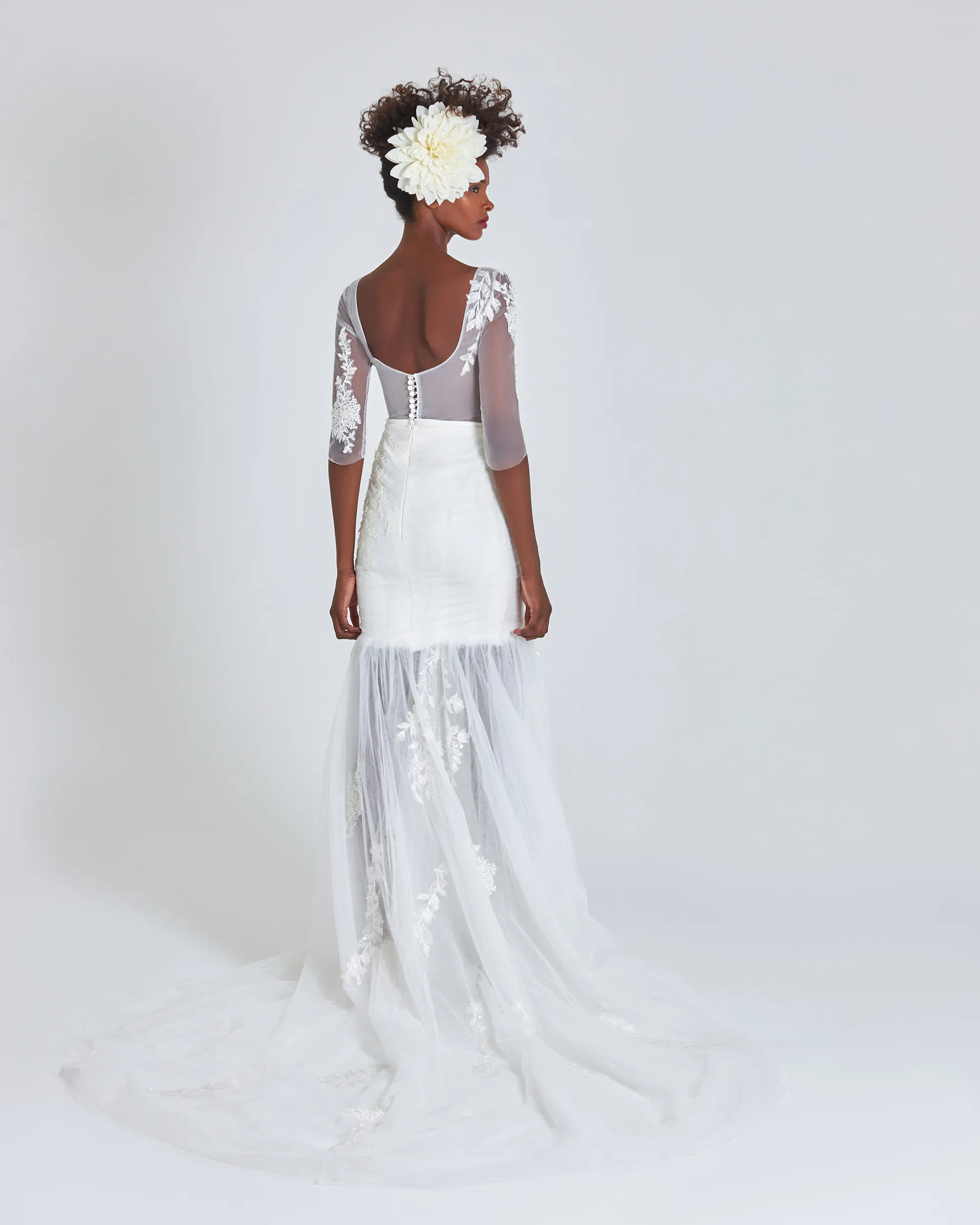 Ife, back: a low scooped illusion back fastened with covered buttons, asymmetric lace on the sleeves and appliqués scattered down the train.