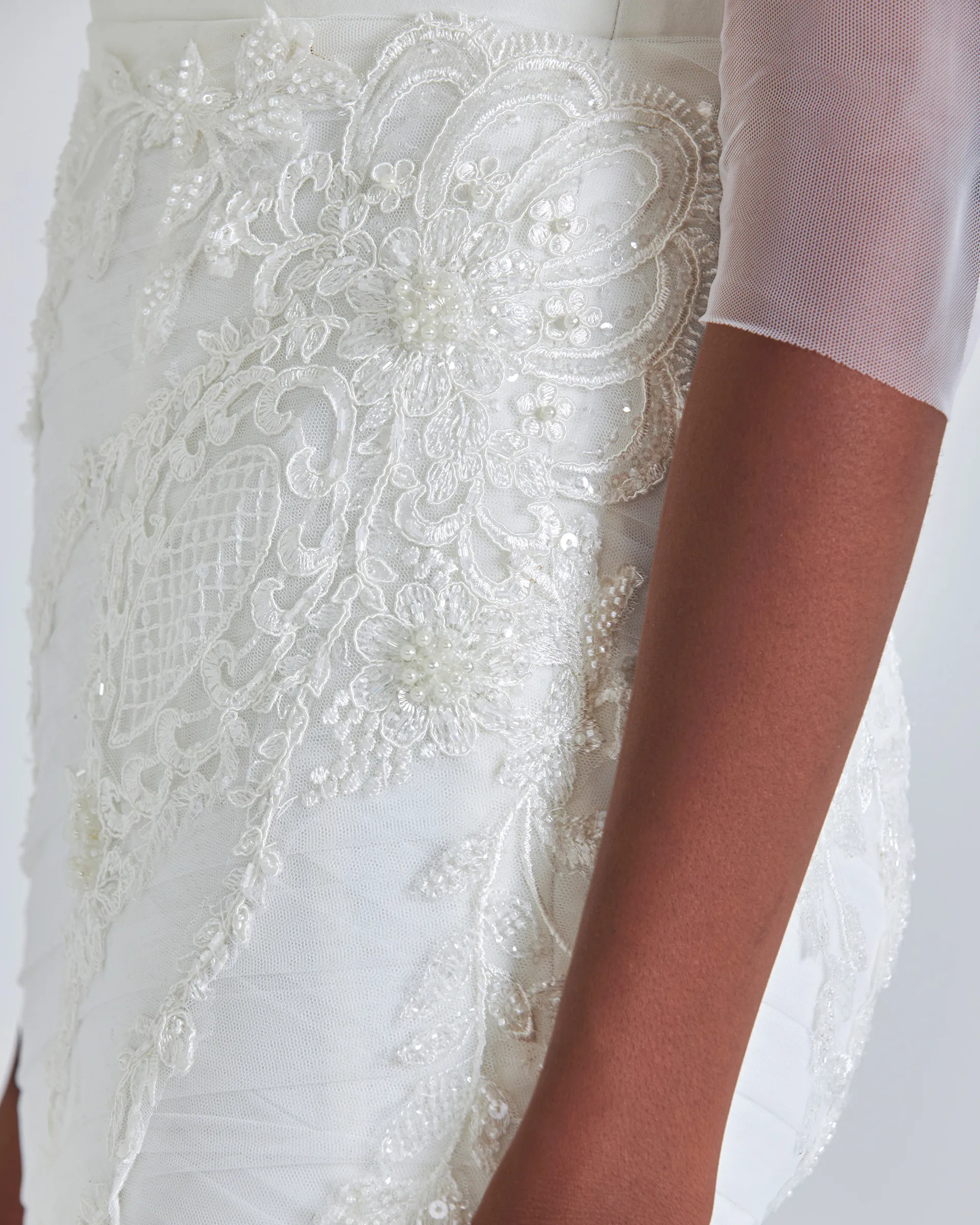 Ife, detail: beaded and corded lace appliqués over the crisscross-draped tulle of the skirt, beside a sheer sleeve.
