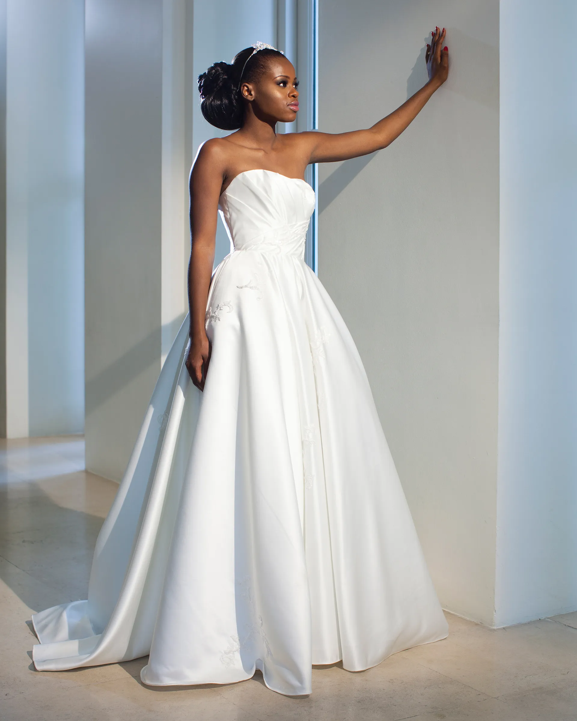 Irina without the sheer top, one hand raised to the wall: the gently shaped strapless neckline, diagonal folds at the waist and the full satin skirt.