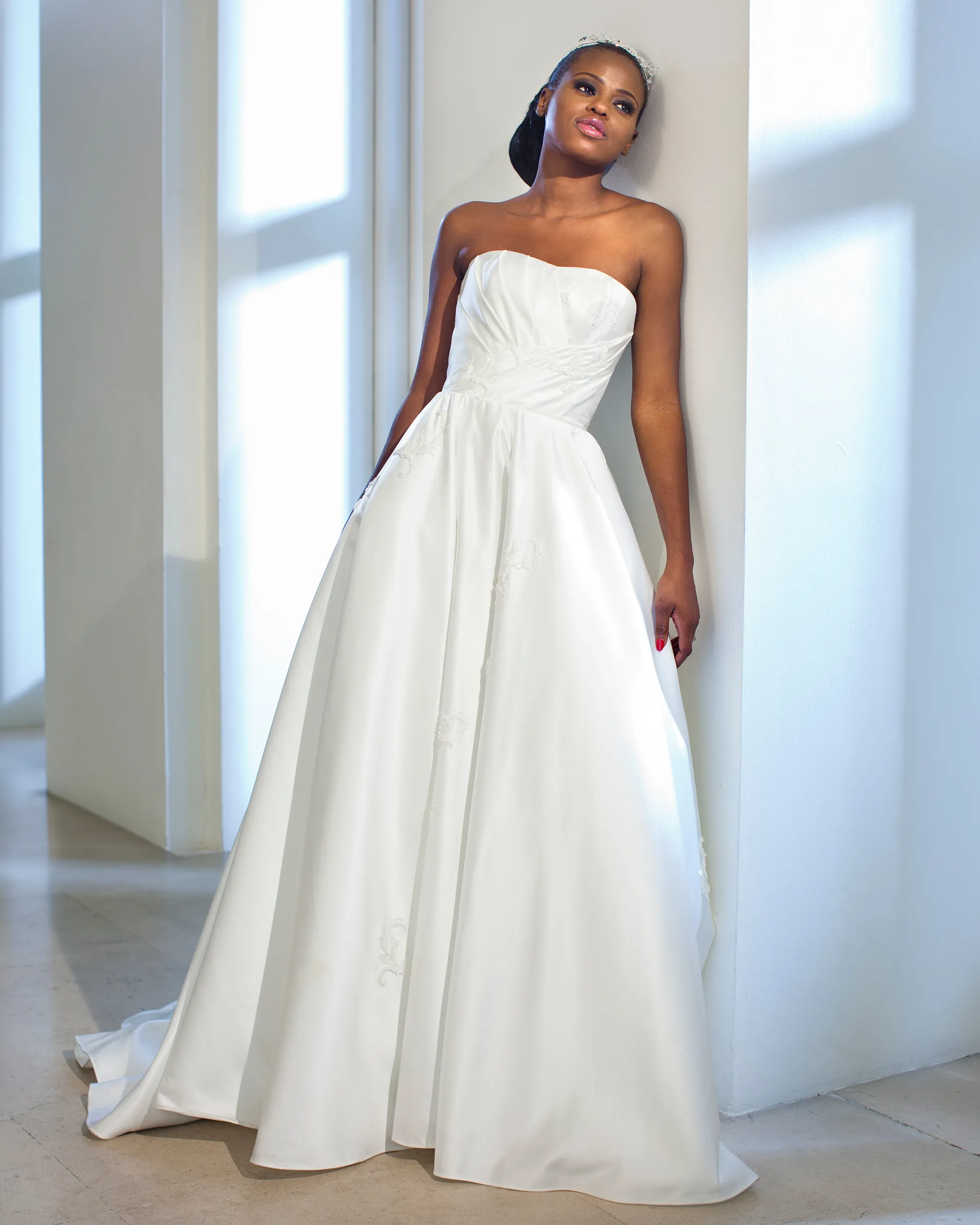 Irina, leaning against a wall: the draped strapless bodice, lace appliqués on the skirt and the satin falling into a short train.