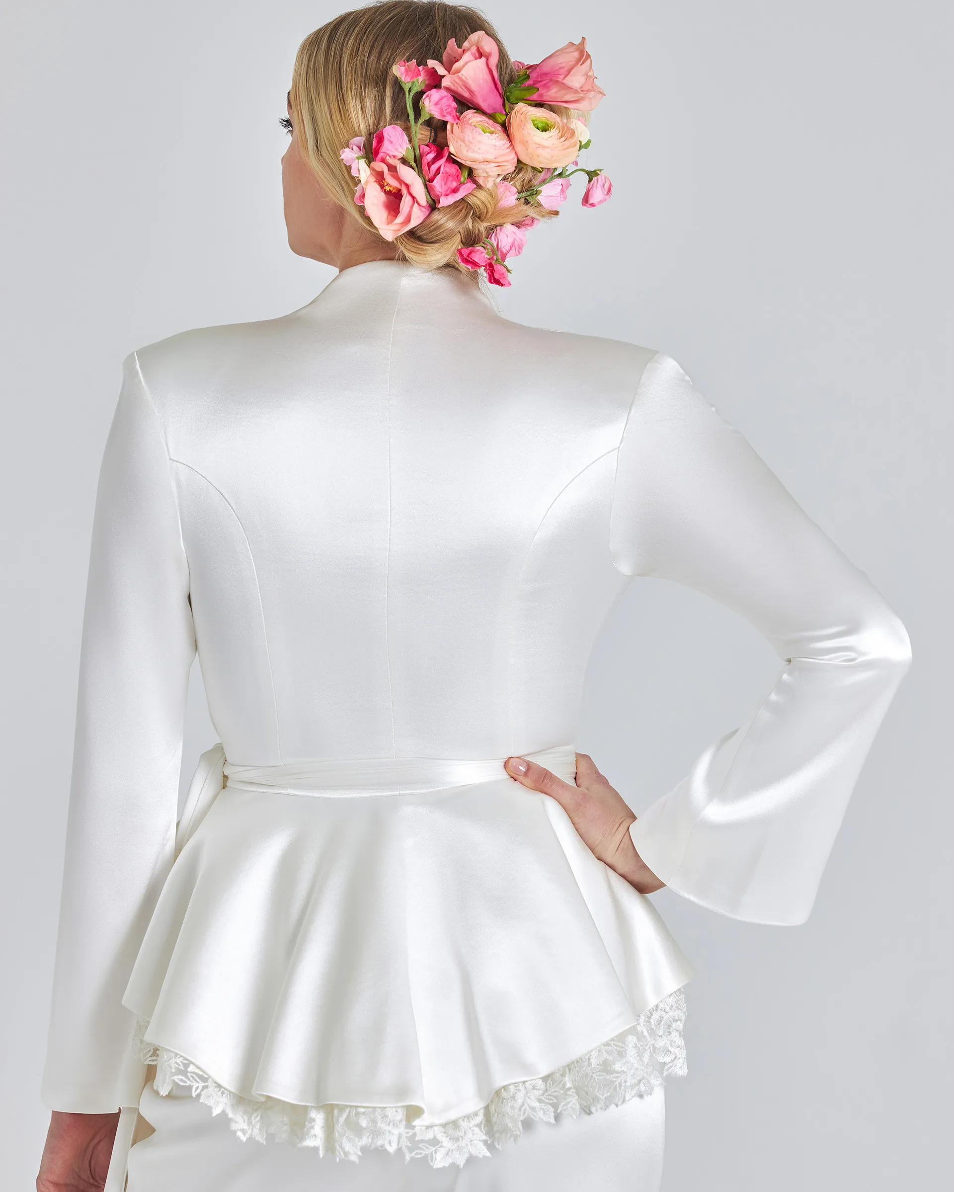 Kemi, back detail: shaped seams through the satin jacket, the tie belt and a peplum edged with scalloped lace; pink roses in her hair.