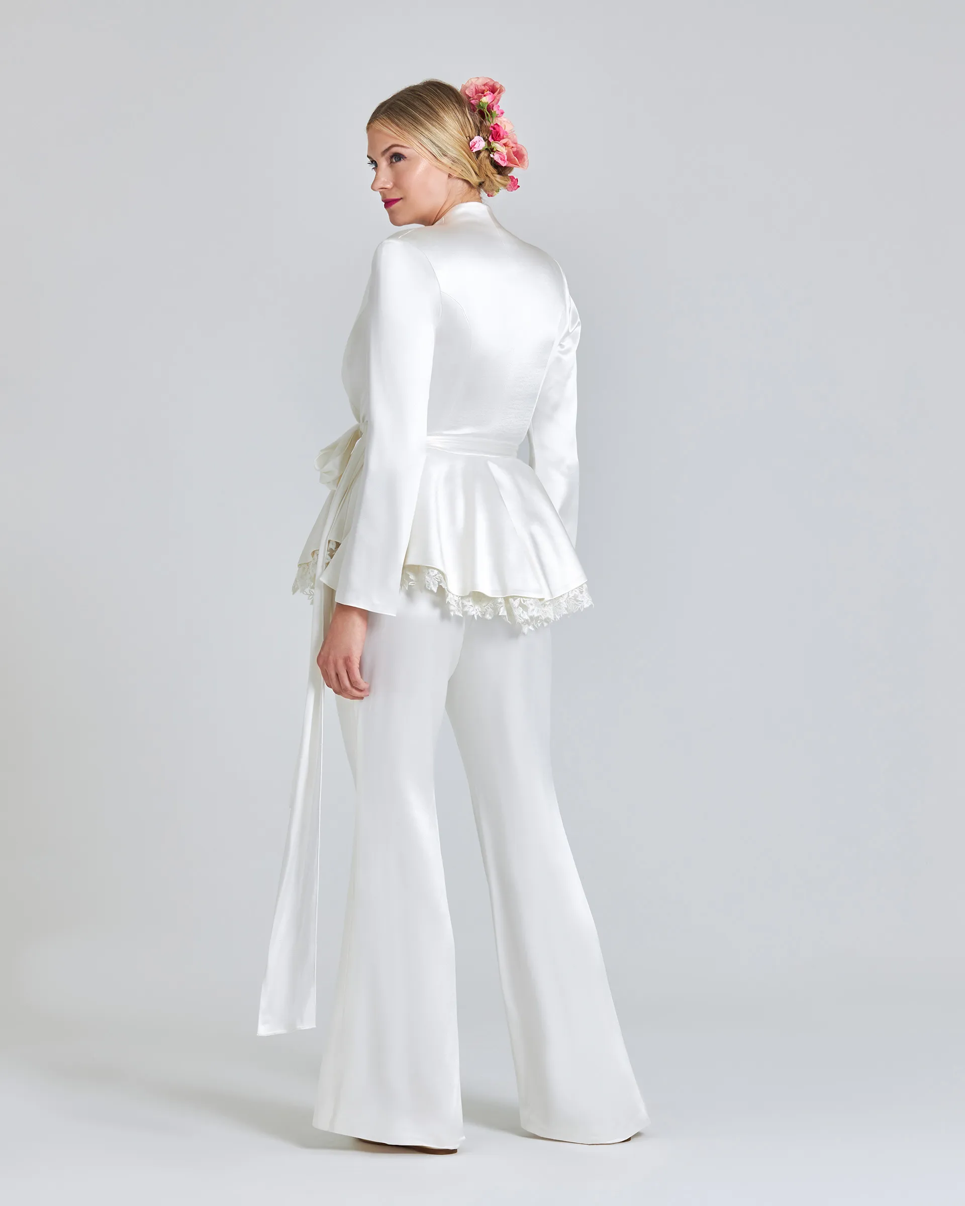 Kemi, back: the fitted satin jacket over its peplum and lace trim, with the trousers flaring slightly to the floor.