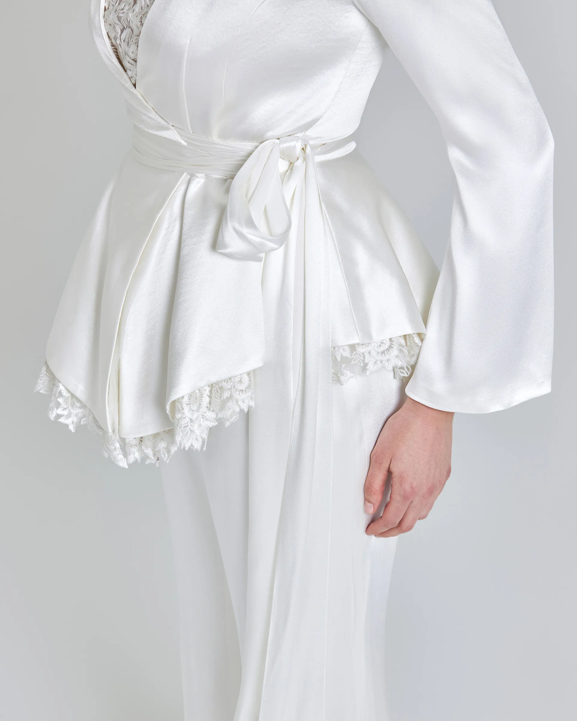 Kemi, side detail: the satin tie knotted at the waist, the peplum flaring over a scalloped lace trim, and a sleeve opening at the cuff.