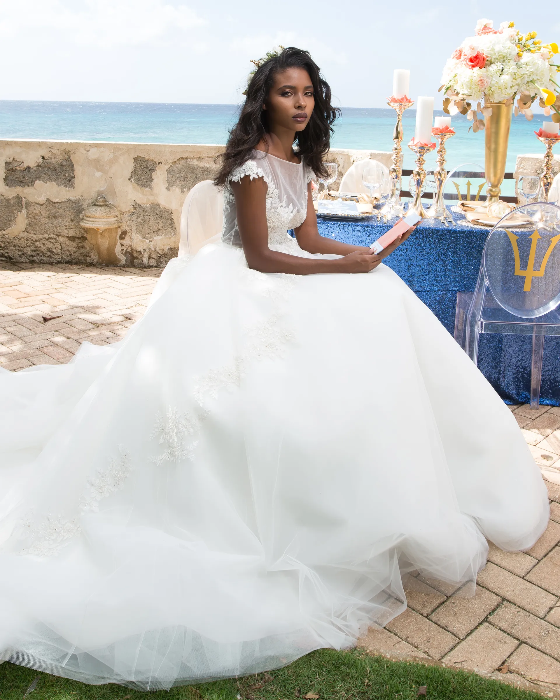 Melpomene seated at a table laid with candles and flowers by the sea, the tulle ballgown skirt billowing around her chair.
