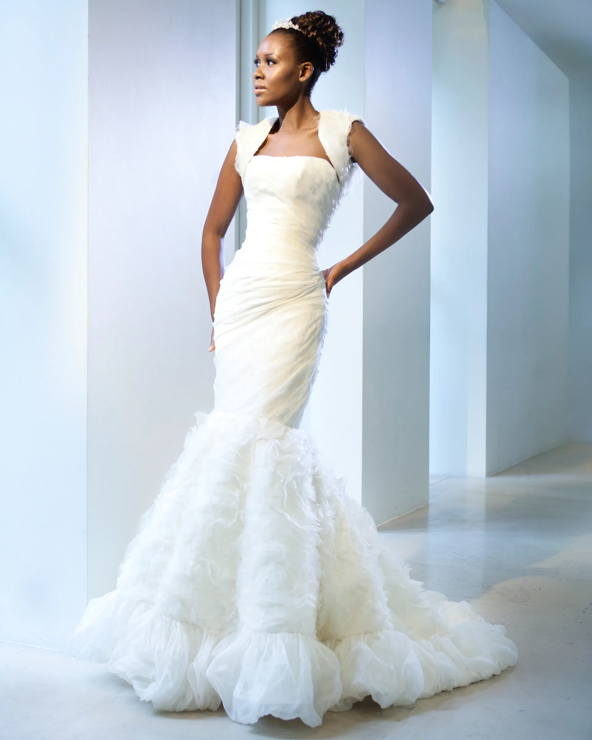 Odette, hands on hips: the textured organza bolero with cap sleeves, the ruched fitted line through the hips and the rose-swirl skirt flaring to a chapel train.