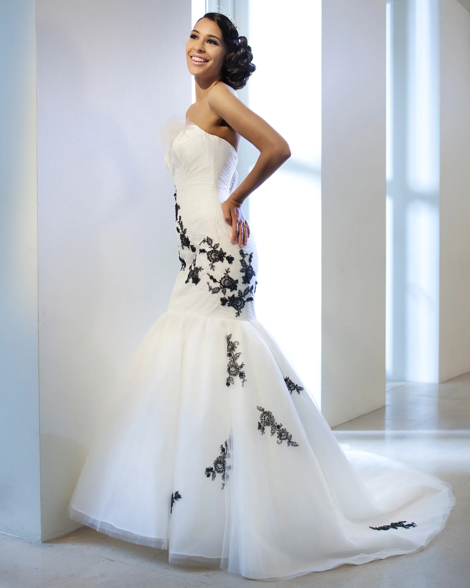Odile, smiling, hand on hip: black lace appliqués scattered asymmetrically over the ruched bodice and down the layered tulle skirt to a chapel train.