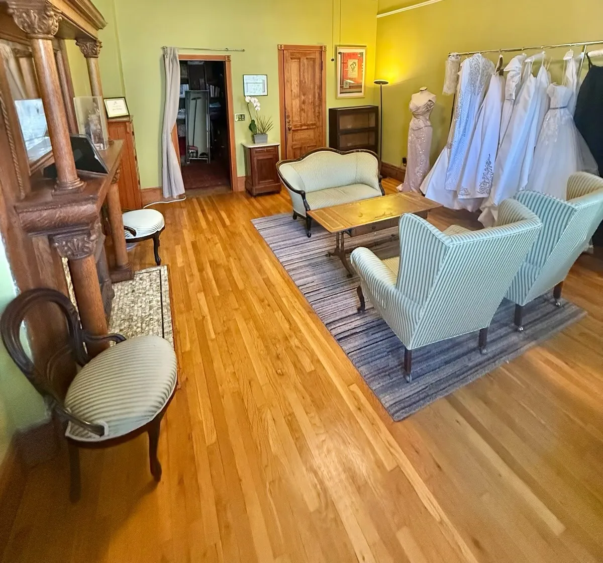 The salon looking toward the doorway, with a carved oak mantel, plaster ceiling and bridal gowns on a rail.