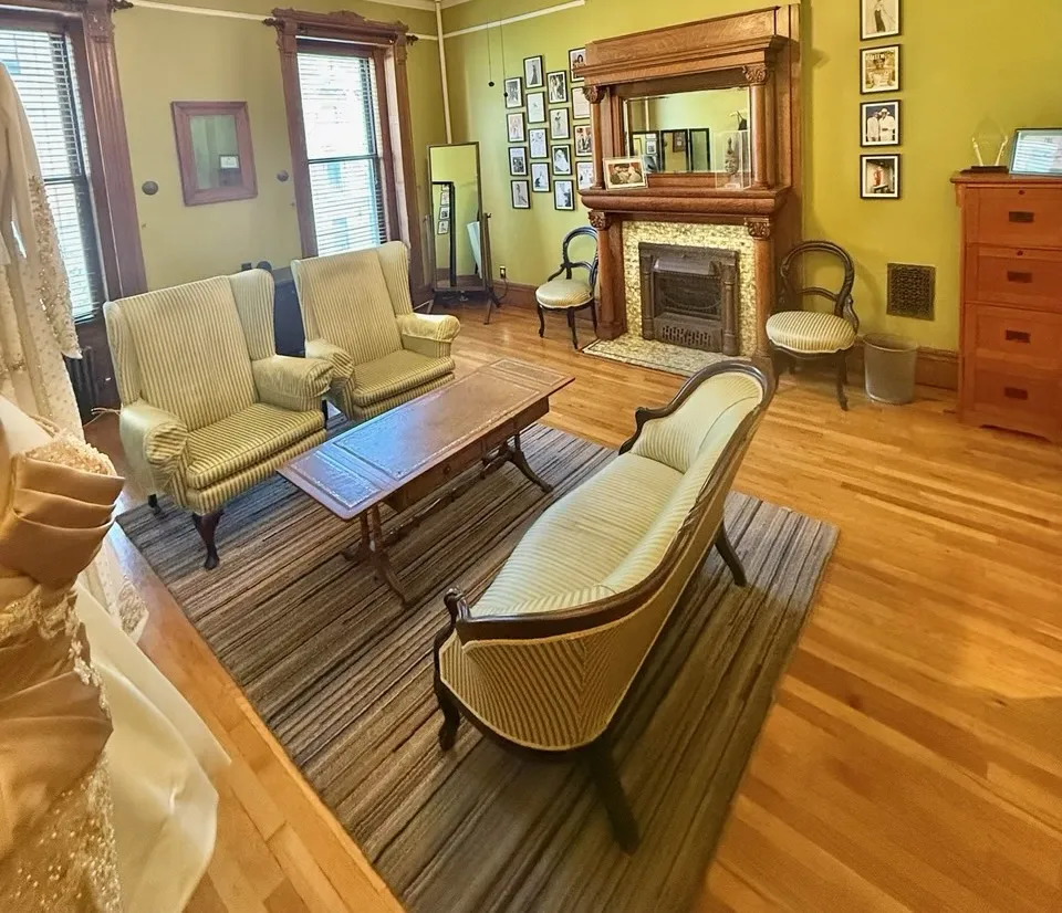 The salon fireplace with its oak overmantel, framed photographs on the walls and a full-length mirror by the window.