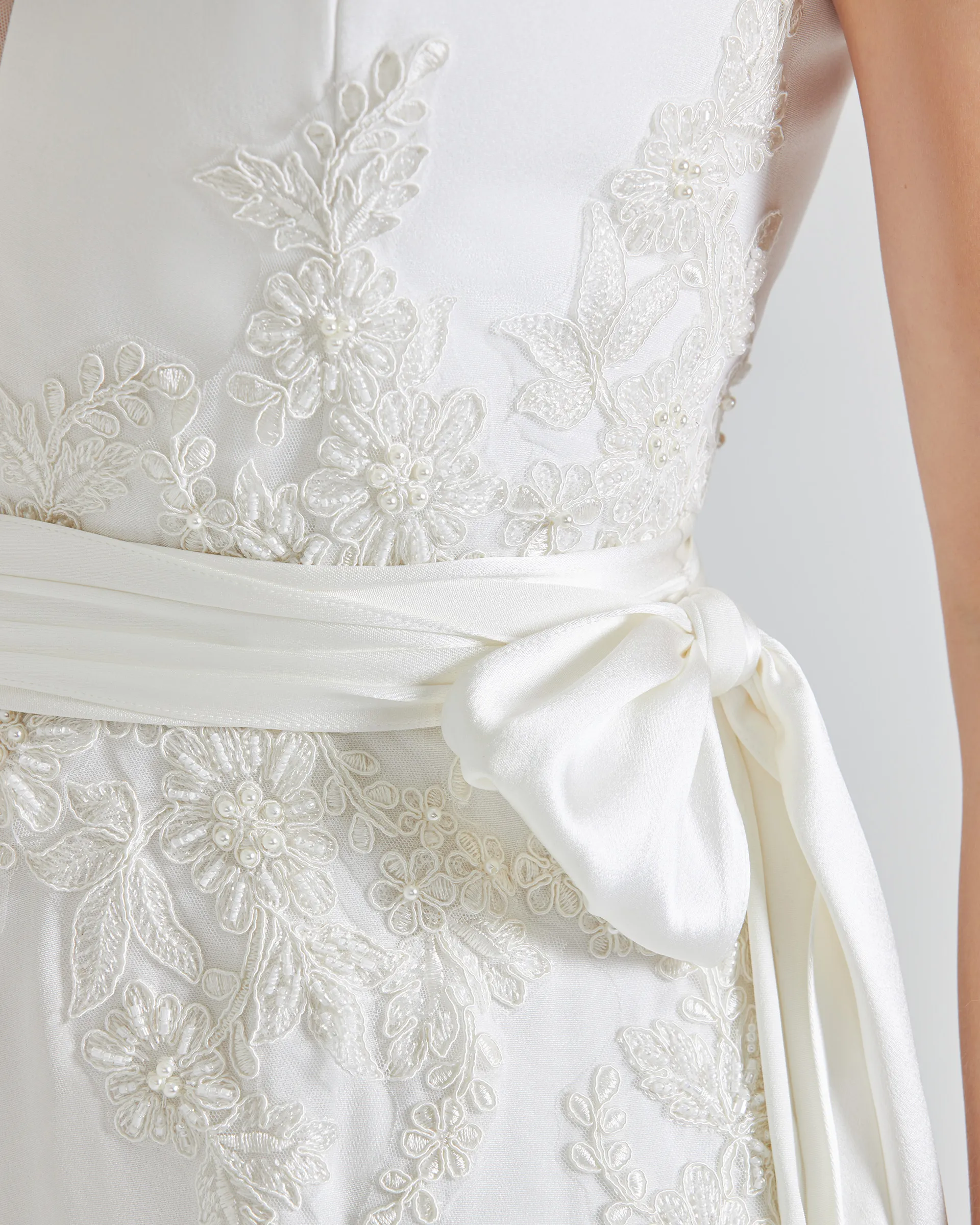 Tinuke, back detail: pearl-beaded lace appliqués above and below the waist, crossed by the satin sash and its bow.
