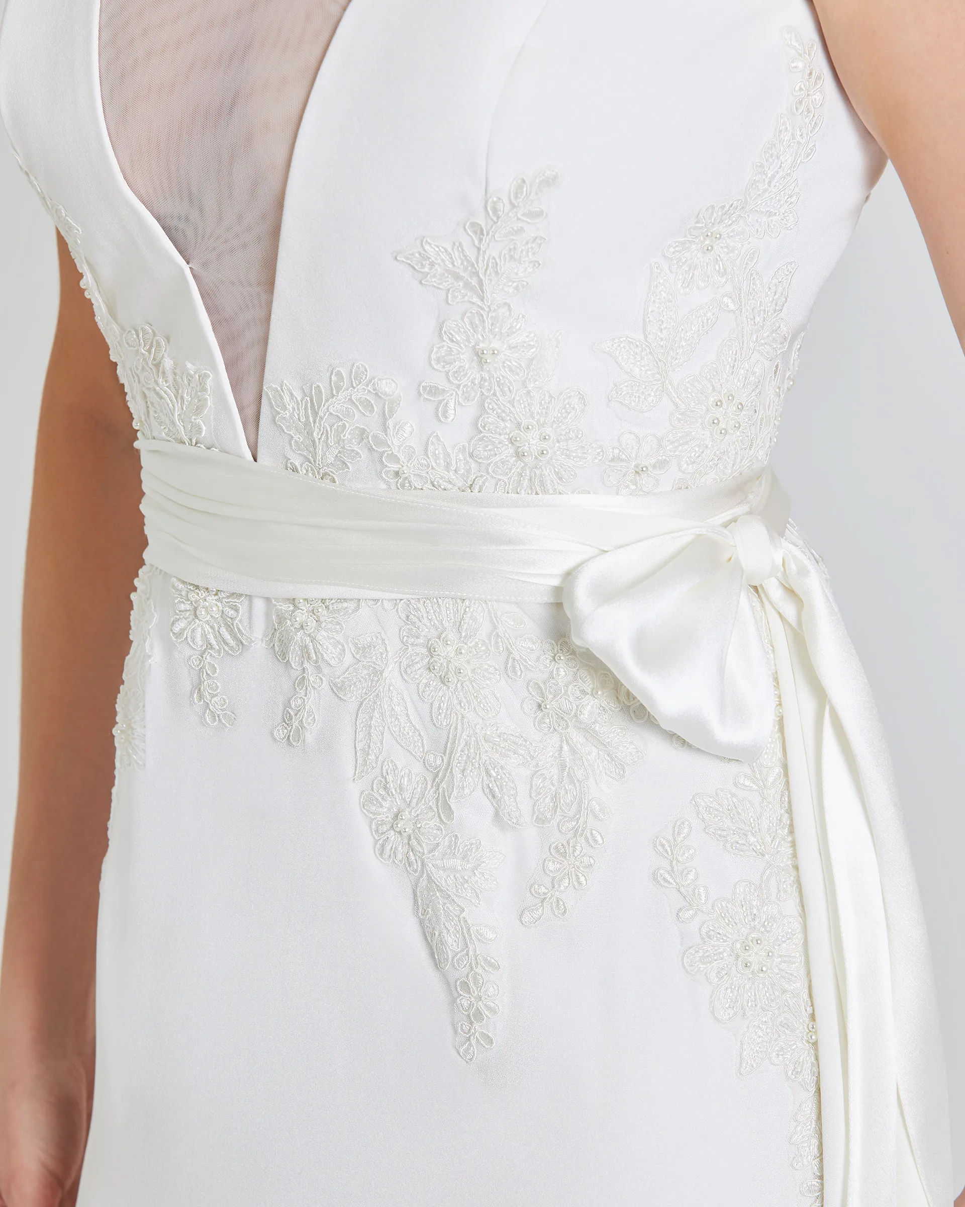 Tinuke, front detail: beaded lace appliqués radiating from the waist, the satin sash knotted into a bow, and the edge of the illusion tulle panel.