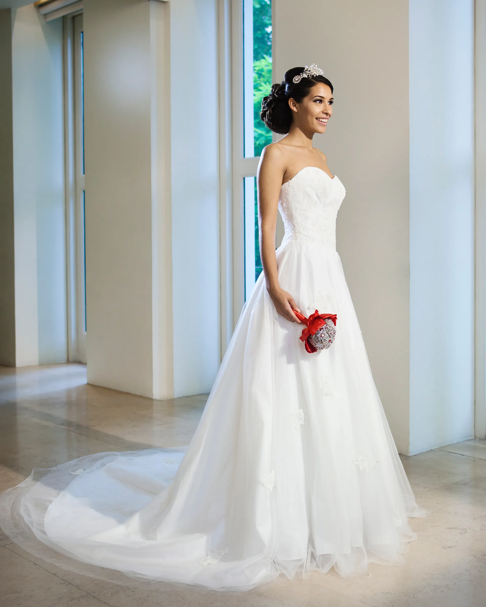 Titania without the chemise, holding a red and crystal brooch bouquet: the strapless lace sweetheart bodice and a circular skirt of layered tulle sweeping into a cathedral train.